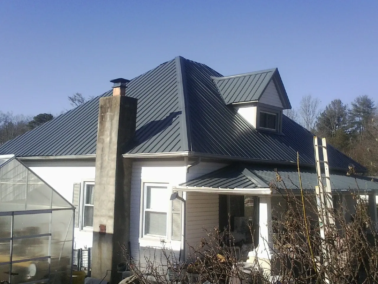 Dark blue standing seam metal roof on a white farmhouse with dormer — Slate & Tile Roof Repair by Roofing Brothers in Mount Rainier