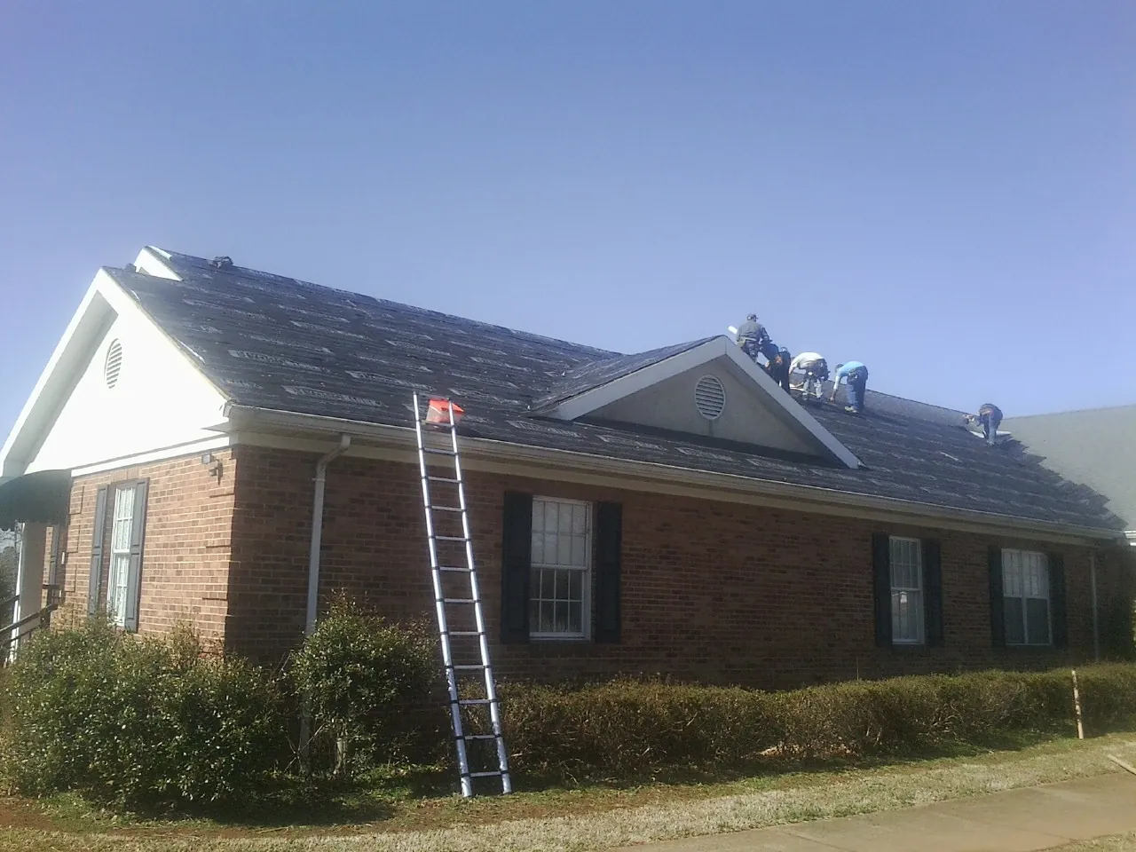 Crew tearing shingles off a brick ranch roof with a ladder set — Emergency Roof Repair work by our crew in Mount Rainier