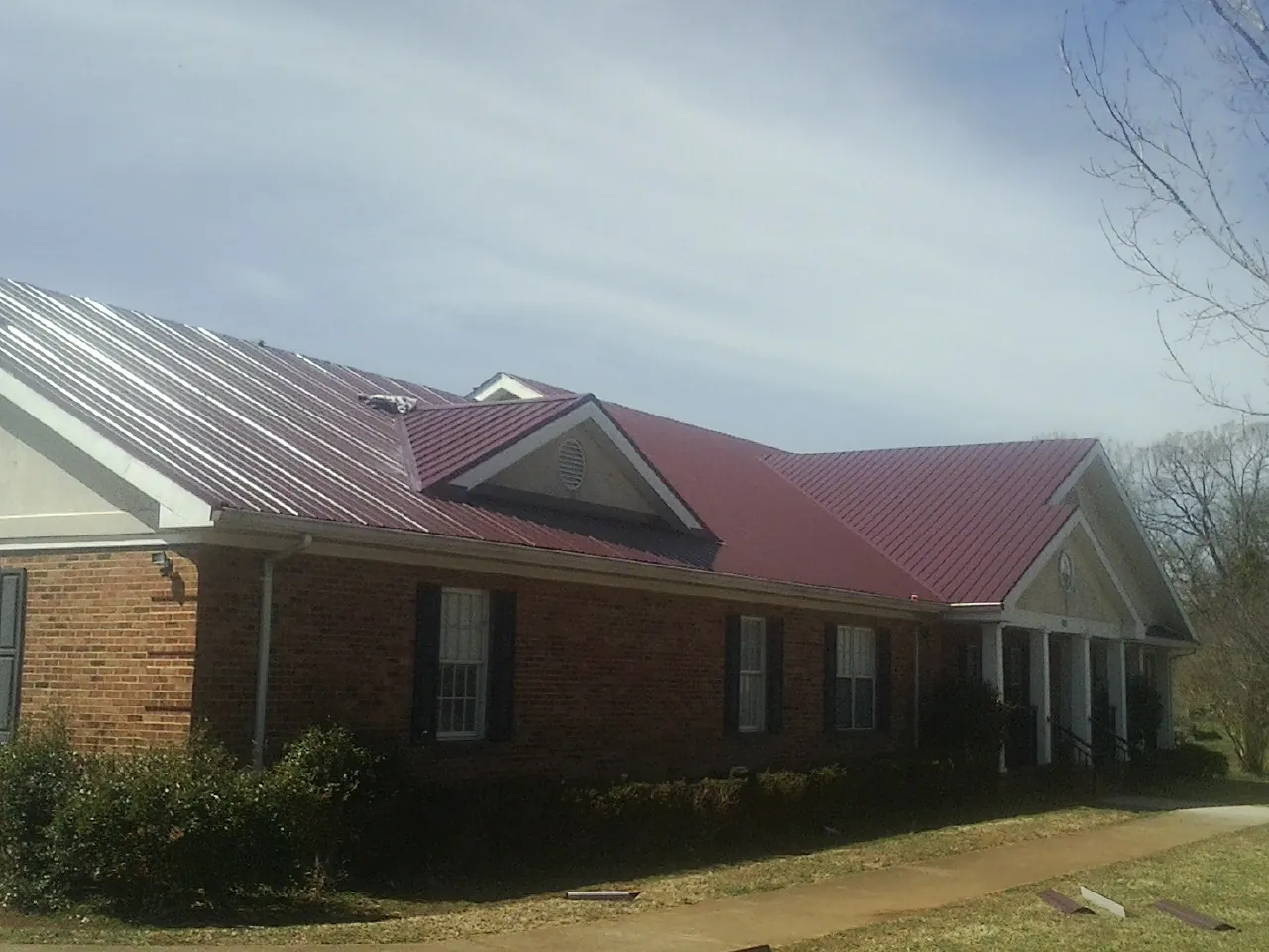 Red metal roof with gabled entries on a long brick building, from a Hail Damage Roof Repair job in Mount Rainier