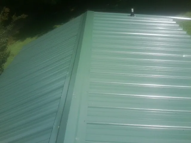 New green metal panels meeting at the ridge of a roof — Flat Roof Repair work by our crew in Mount Rainier