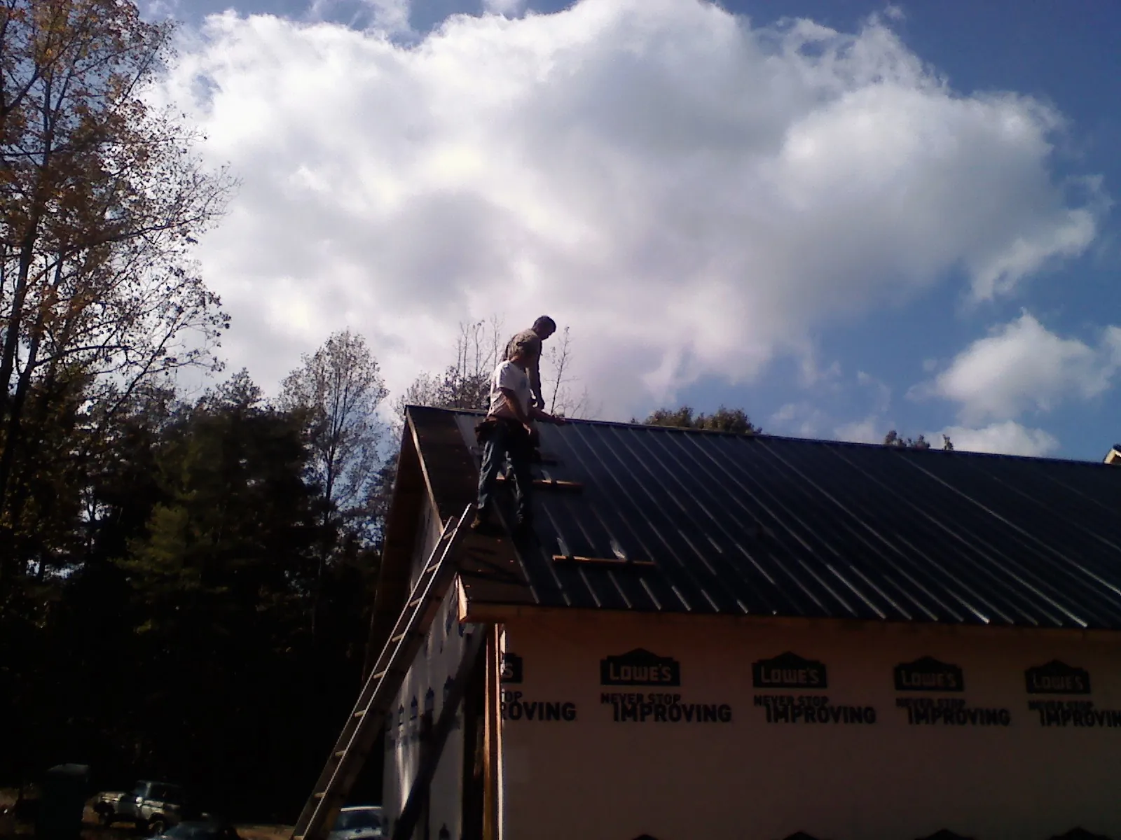 Roofer fastening dark metal panels high against a cloudy sky, from a Roof Inspection job in Mount Rainier