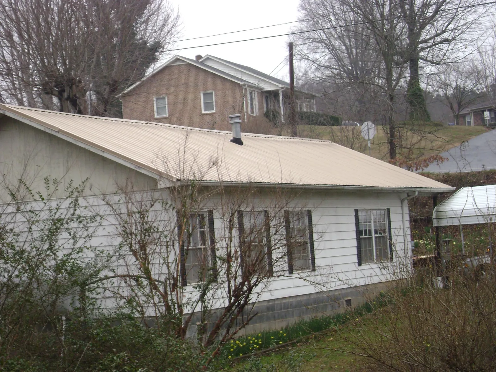 Tan metal roof on a white sided house set into a hillside — Commercial Roofing by Roofing Brothers in Mount Rainier